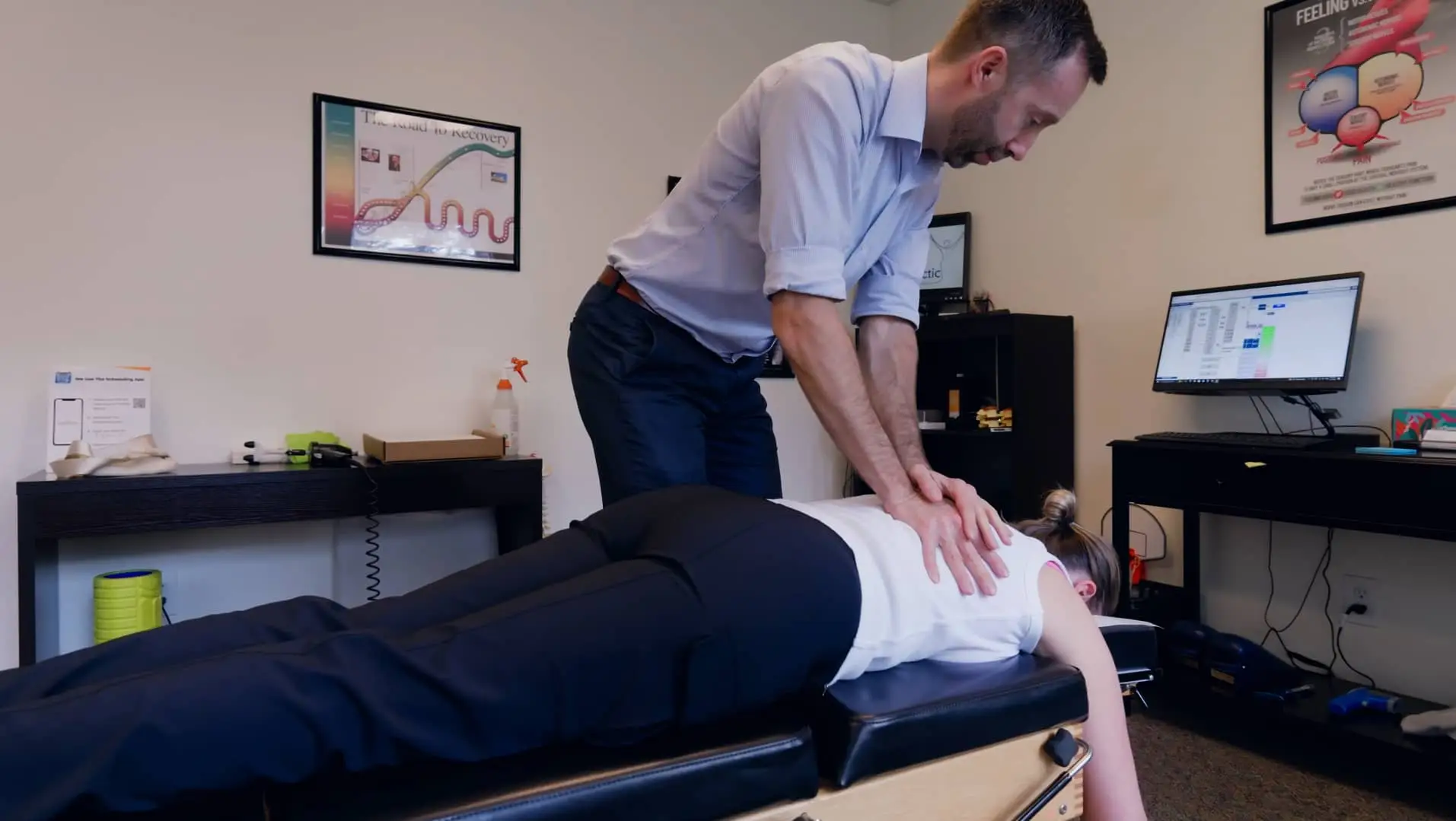 A chiropractor adjusts a female patient's upper back on a chiropractic table in an office setting.