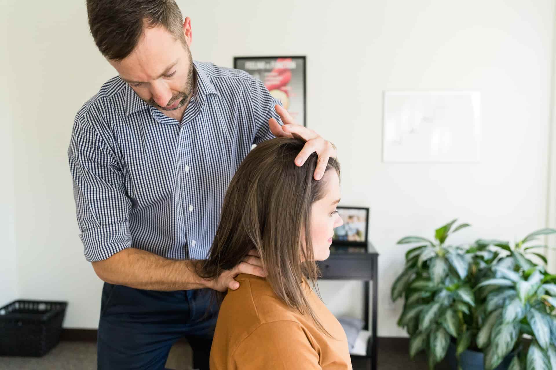 A man with a beard in a striped shirt adjusts a woman's head and neck.