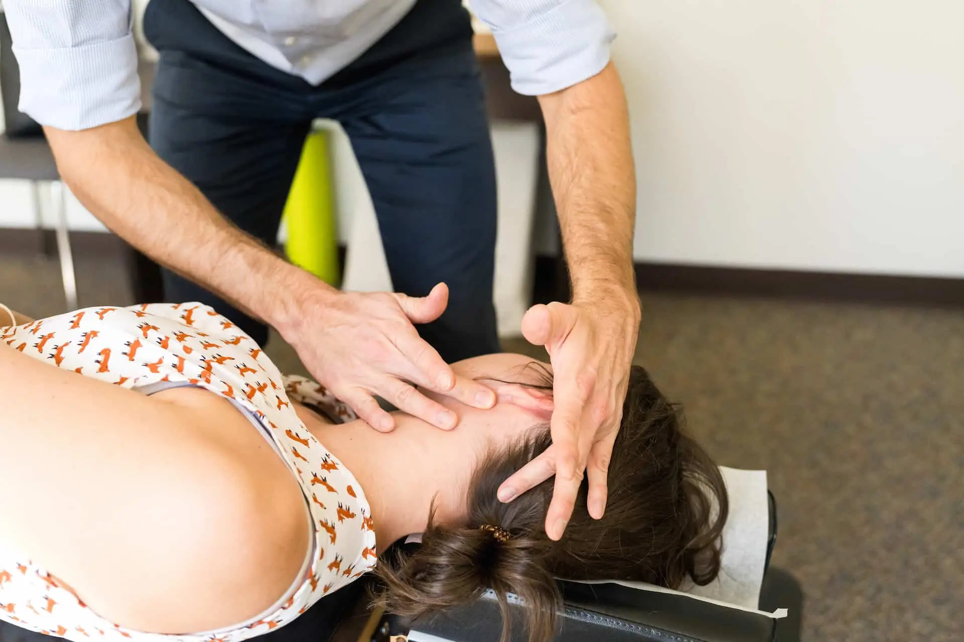 A practitioner's hands adjusting the neck and head of a person lying on an examination table.