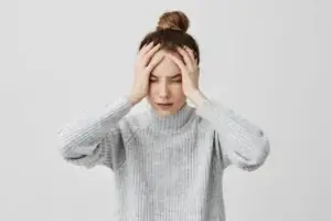 A woman with her eyes closed, holding her head with both hands, looking distressed.