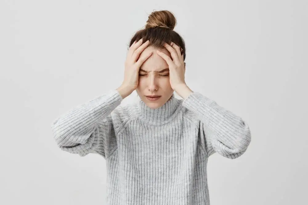 A woman with her eyes closed, holding her head with both hands, looking distressed.