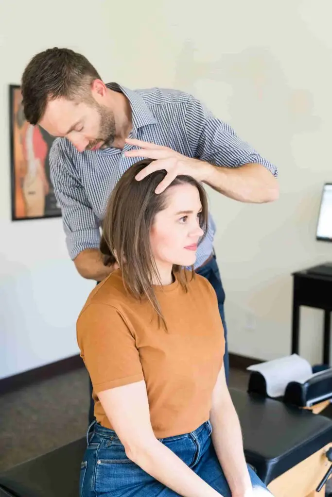 A male chiropractor adjusts the neck of a female patient who is seated.
