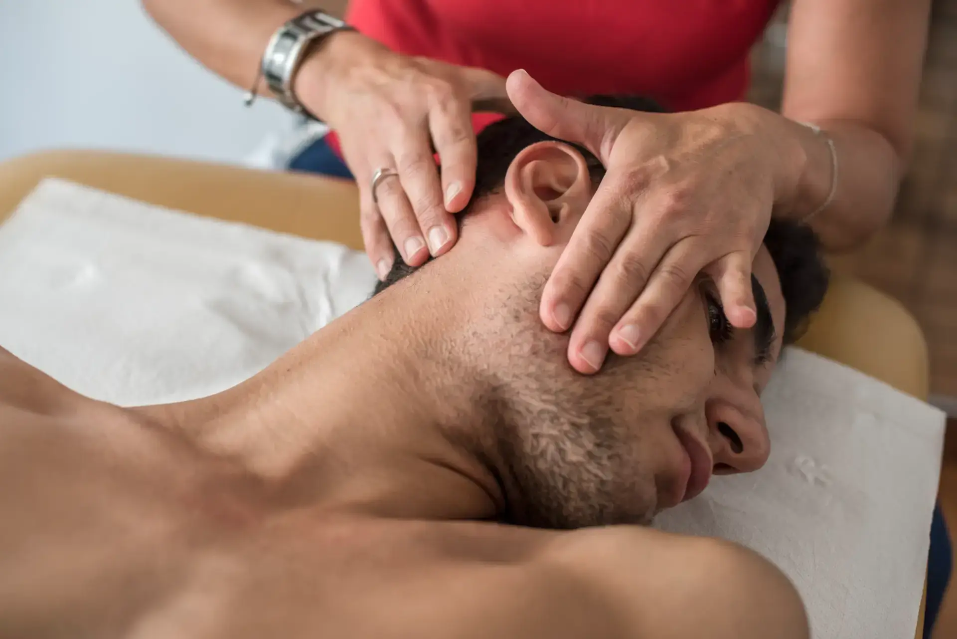 Close-up of a person receiving a head and neck massage from another person's hands.